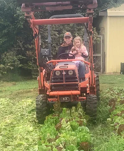 Father and daughter joyfully ride a bright orange tractor in a lush family garden.