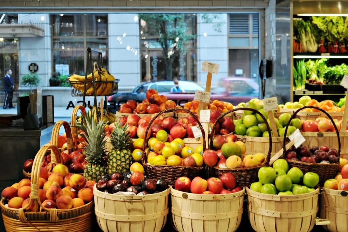 Vibrant fruit market display with fresh apples, peaches, bananas, and pineapples in baskets.